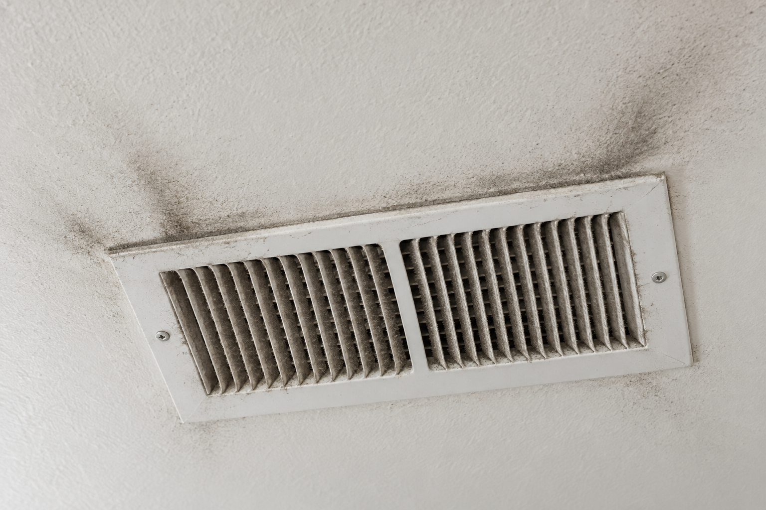 Ceiling supply register with grey dust matted on its louvers and streaks on the ceiling around it